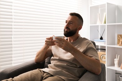 Photo of Harmony. Man with cup of drink in armchair at home