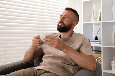 Photo of Harmony. Man with cup of drink in armchair at home