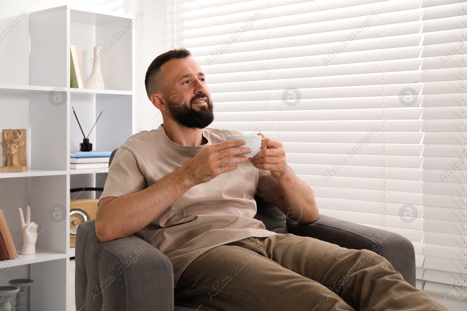 Harmony. Man with cup of drink in armchair at home Photo of Harmony. Man with cup of drink in armchair at home
