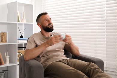 Photo of Harmony. Man with cup of drink in armchair at home