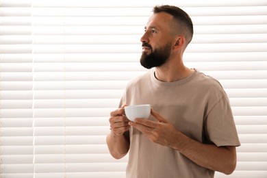 Photo of Harmony. Man with cup of drink near window at home