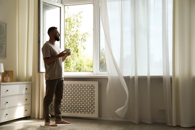Photo of Harmony. Man with cup of drink near window at home