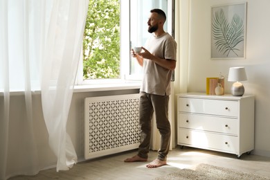 Photo of Harmony. Man with cup of drink near window at home