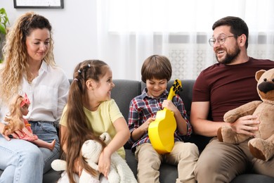 Photo of Children and their parents playing with different toys on sofa at home