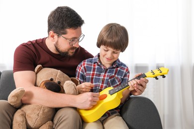Photo of Father and his son playing toy guitar on sofa at home