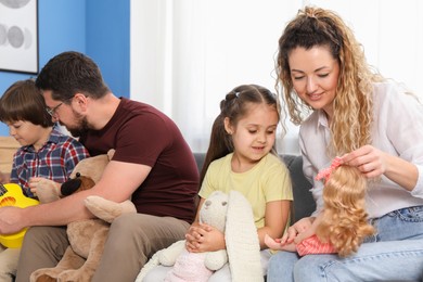 Photo of Children and their parents playing with different toys on sofa at home