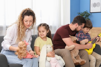 Photo of Children and their parents playing with different toys on sofa at home