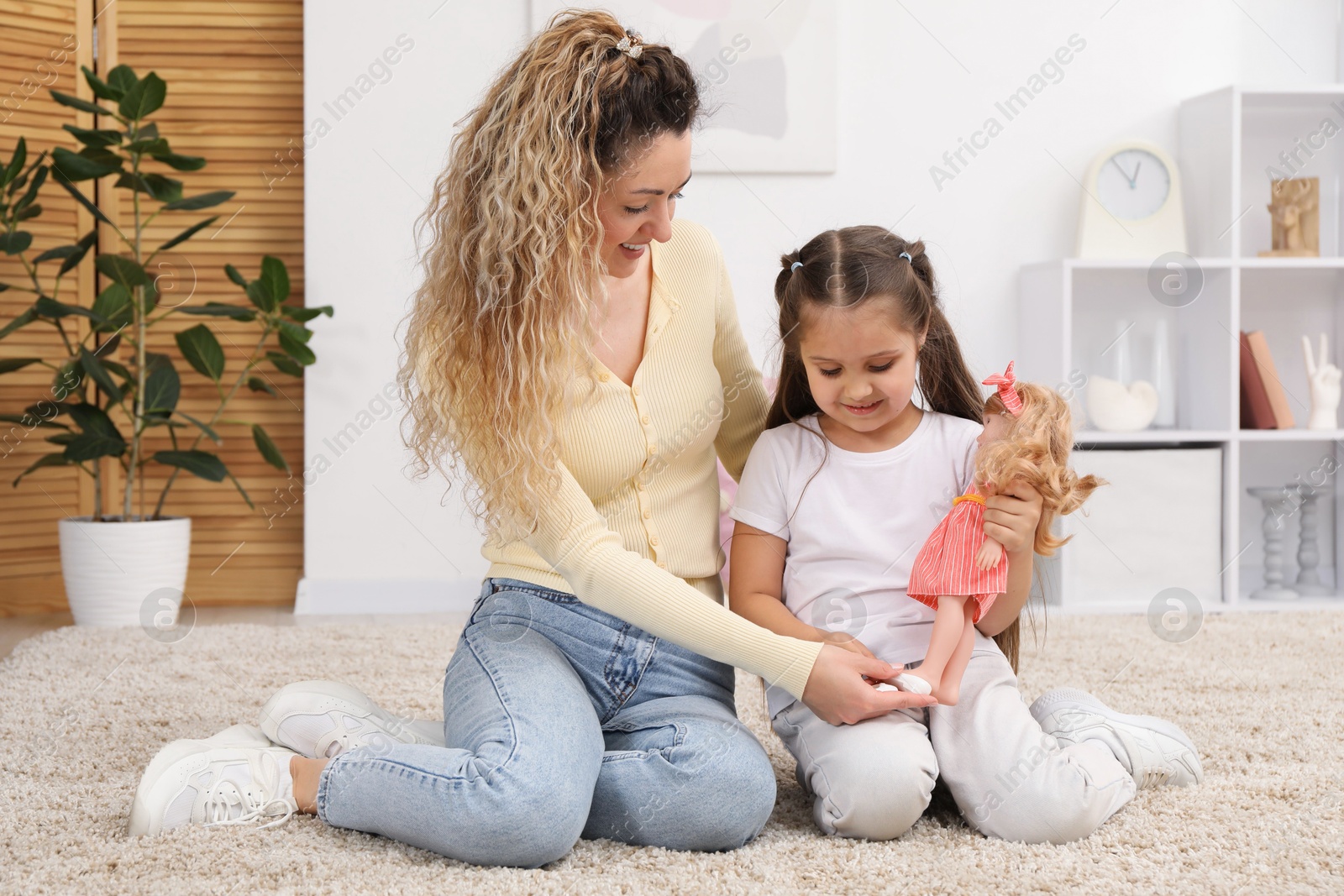 Mother and her daughter playing with doll on floor at home Photo of Mother and her daughter playing with doll on floor at home