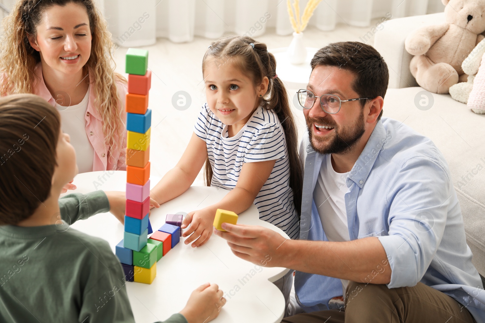 Children and their parents building tower with colorful cubes at white table indoors Photo of Children and their parents building tower with colorful cubes at white table indoors