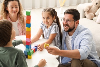 Photo of Children and their parents building tower with colorful cubes at white table indoors