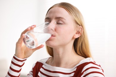 Photo of Young woman drinking water from glass at home, closeup