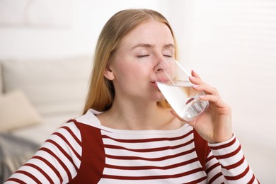 Photo of Young woman drinking water from glass at home