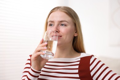 Photo of Young woman drinking water from glass at home