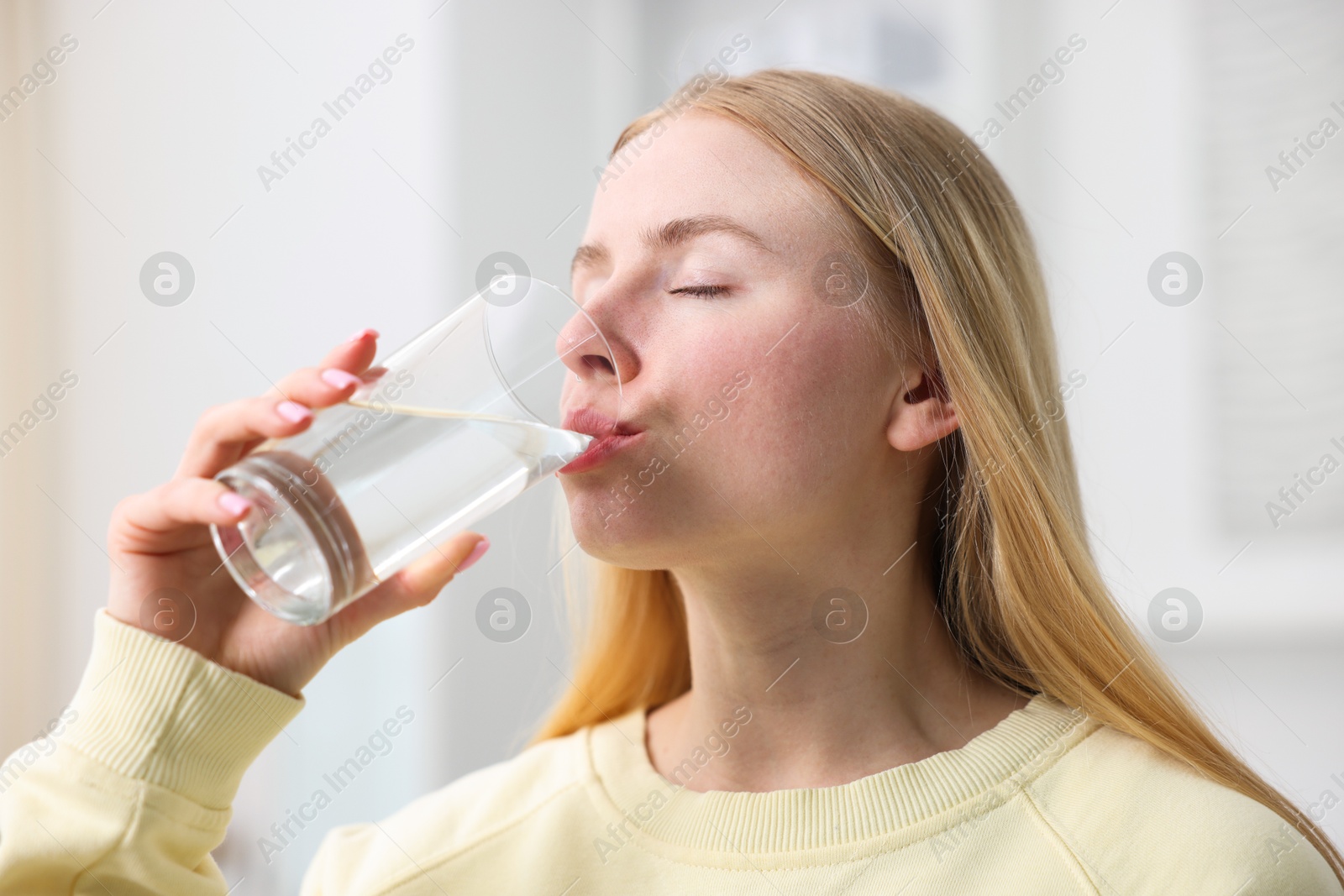 Young woman drinking water from glass at home Photo of Young woman drinking water from glass at home