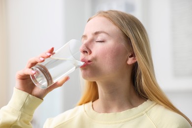 Photo of Young woman drinking water from glass at home