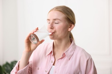 Photo of Young woman drinking water from glass at home