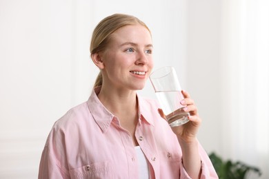 Photo of Young woman drinking water from glass at home
