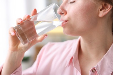 Photo of Young woman drinking water from glass at home, closeup