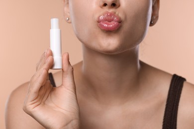 Photo of Young woman with lip balm on beige background, closeup