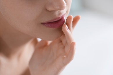 Photo of Young woman with lip balm at home, closeup. Space for text