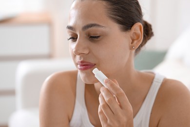Photo of Young woman with lip balm at home