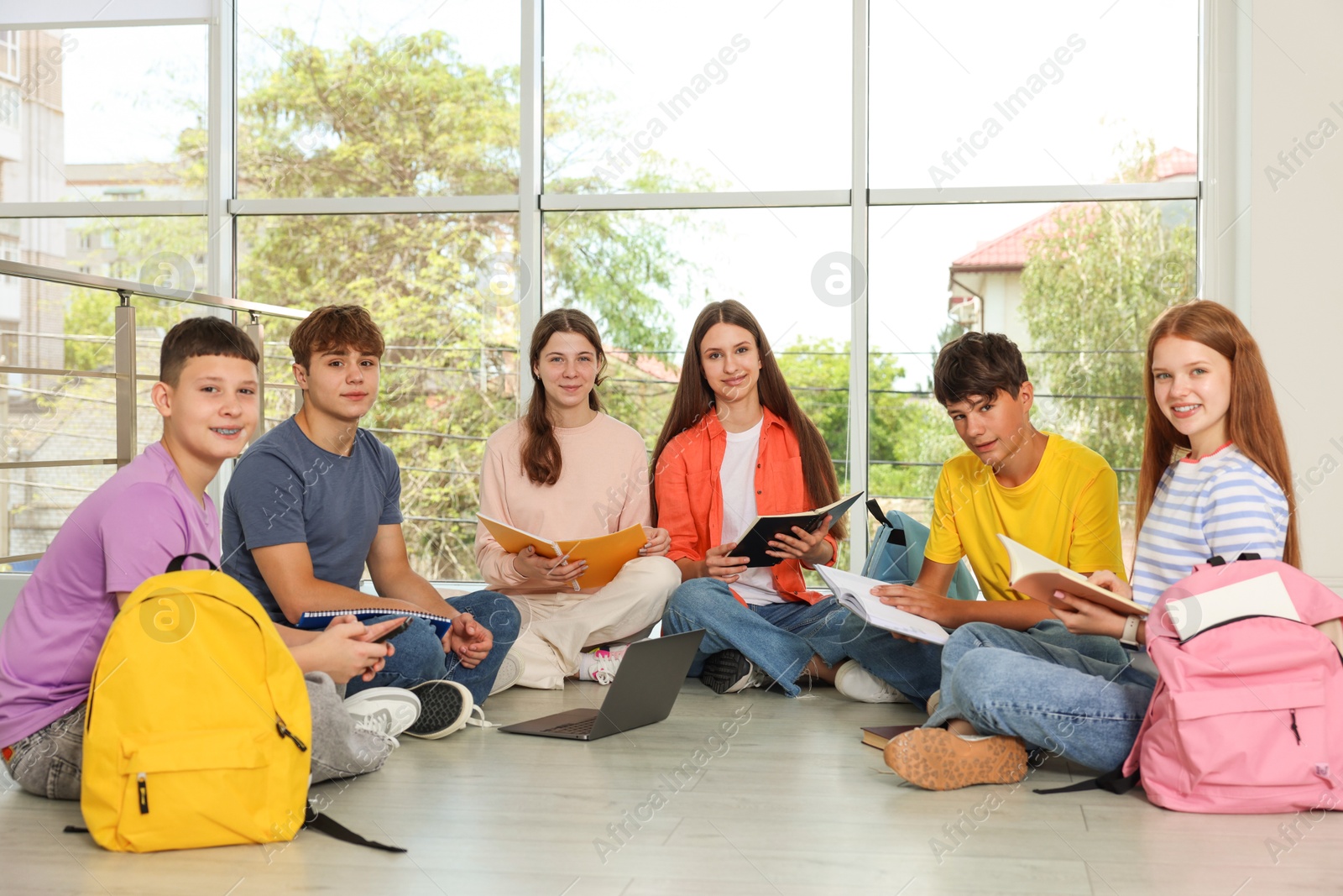 Photo of Group of teenagers with notebooks and laptop studying together indoors