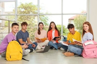 Photo of Group of teenagers with notebooks and laptop studying together indoors