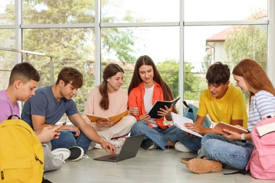 Photo of Group of teenagers with notebooks and laptop studying together indoors