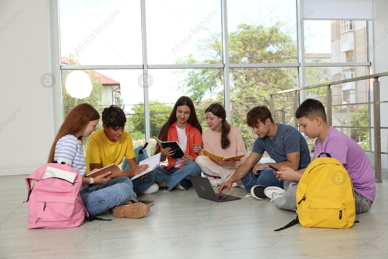 Group of teenagers with notebooks and laptop studying together indoors Photo of Group of teenagers with notebooks and laptop studying together indoors