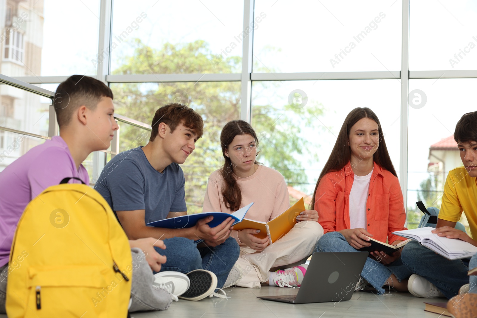Group of teenagers with notebooks and laptop studying together indoors Photo of Group of teenagers with notebooks and laptop studying together indoors