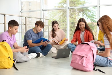 Photo of Group of teenagers with notebooks and laptop studying together indoors