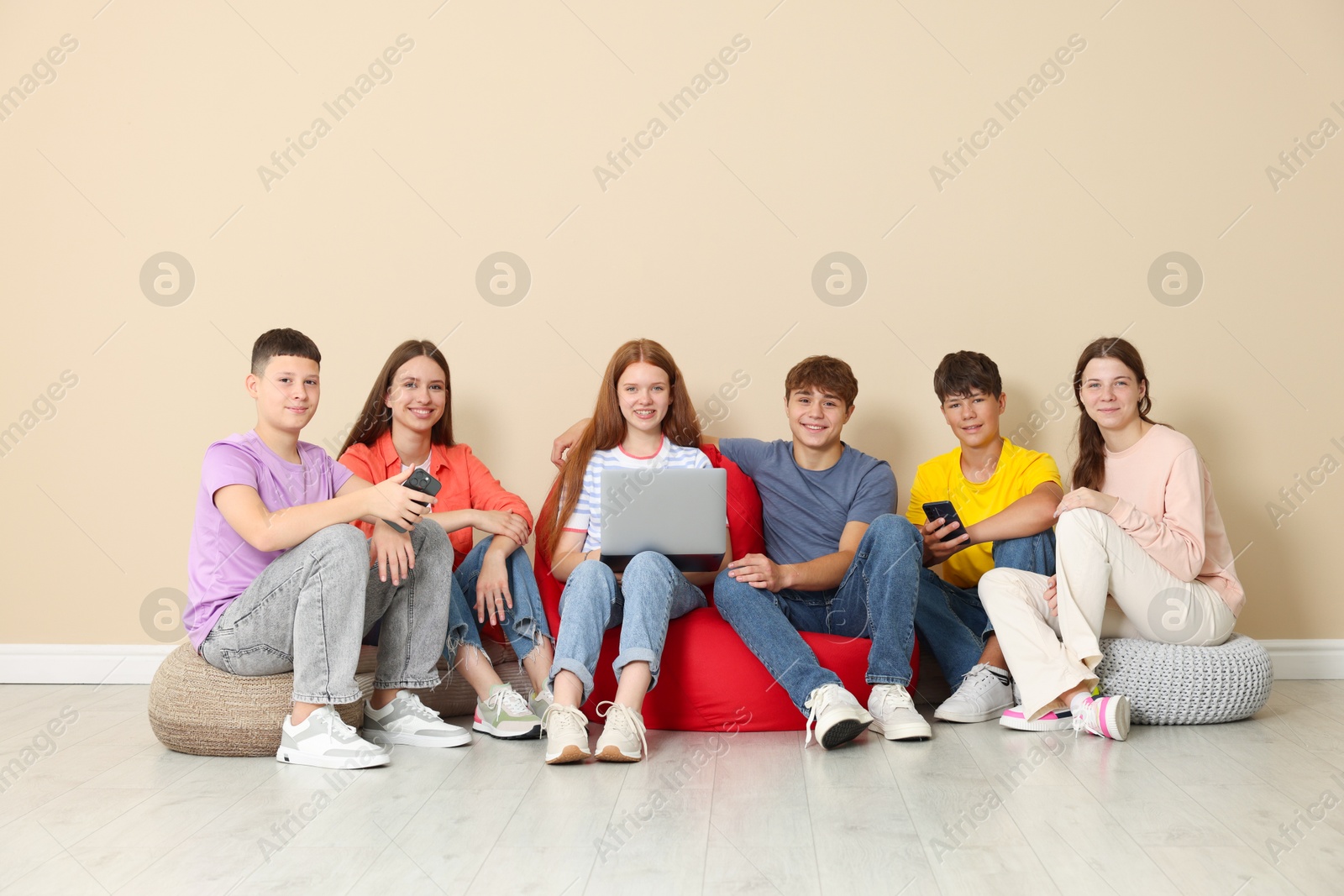 Group of teenagers with laptop and smartphones on bean bags indoors Photo of Group of teenagers with laptop and smartphones on bean bags indoors
