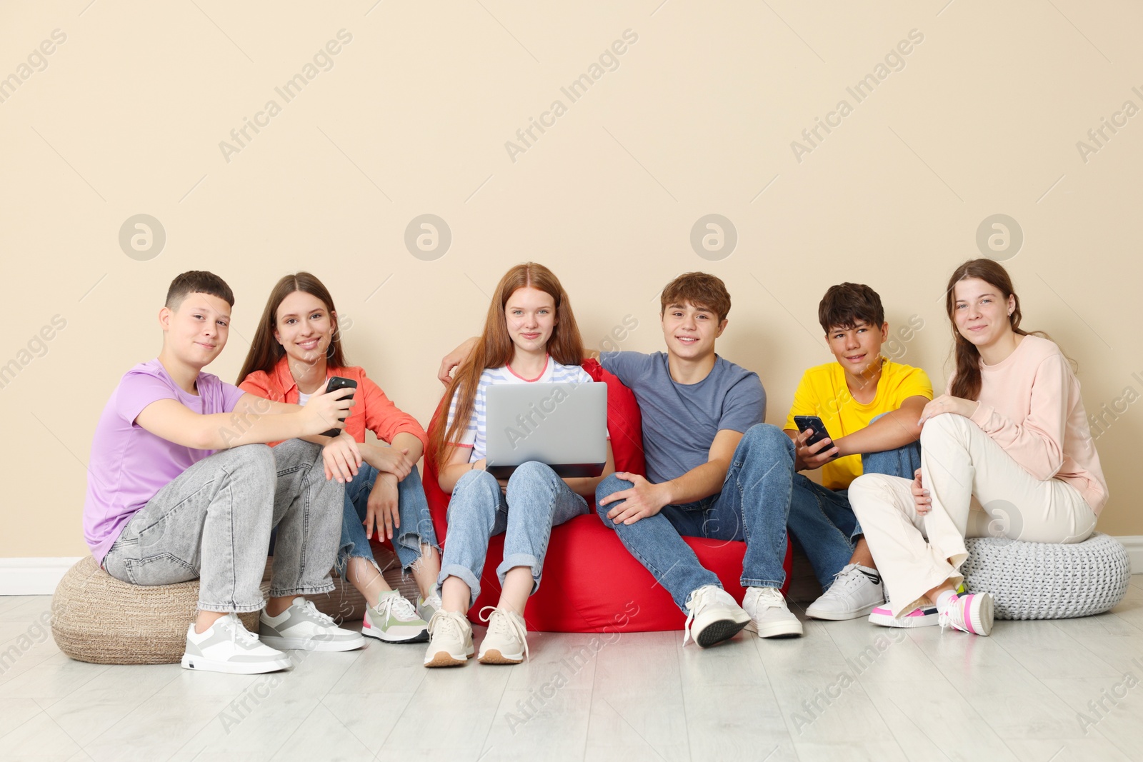 Group of teenagers with laptop and smartphones on bean bags indoors Photo of Group of teenagers with laptop and smartphones on bean bags indoors