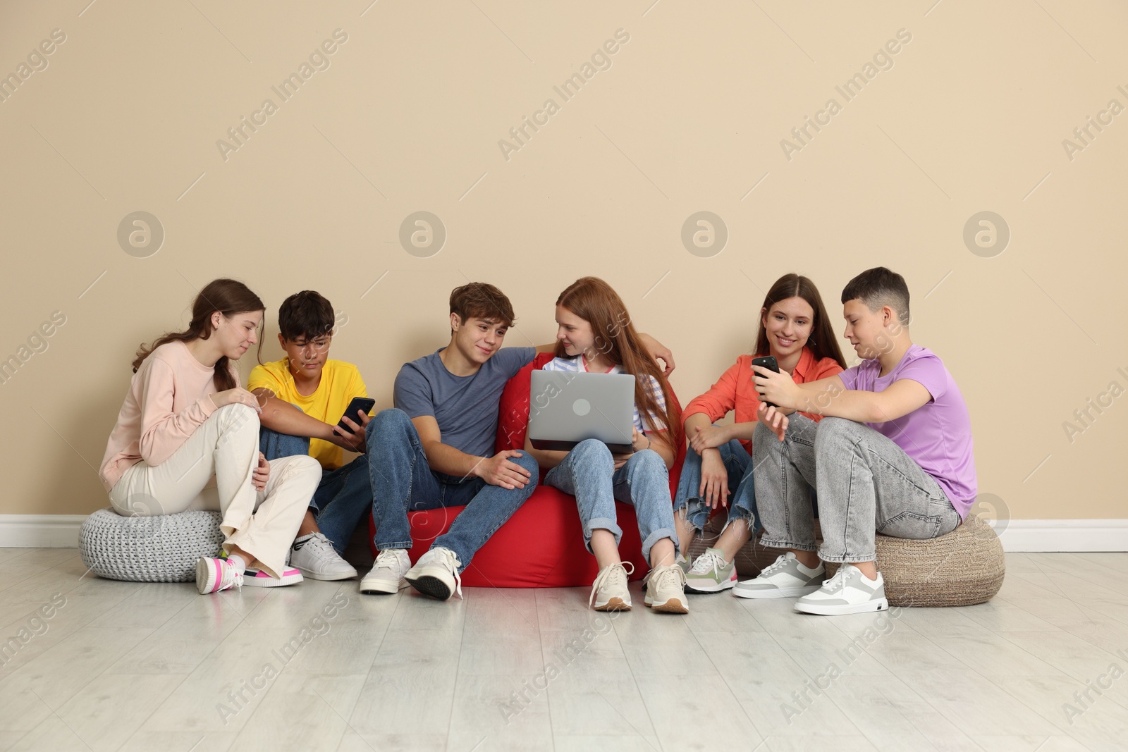 Group of teenagers with laptop and smartphones on bean bags indoors Photo of Group of teenagers with laptop and smartphones on bean bags indoors