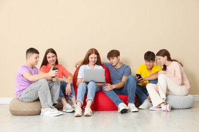 Photo of Group of teenagers with laptop and smartphones on bean bags indoors
