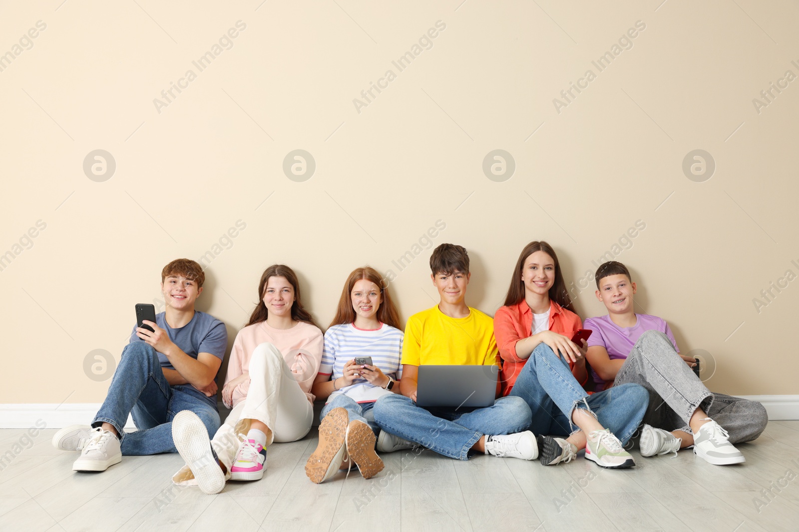Group of teenagers with laptop and smartphones near beige wall indoors. Space for text Photo of Group of teenagers with laptop and smartphones near beige wall indoors. Space for text