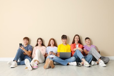 Photo of Group of teenagers with laptop and smartphones near beige wall indoors. Space for text