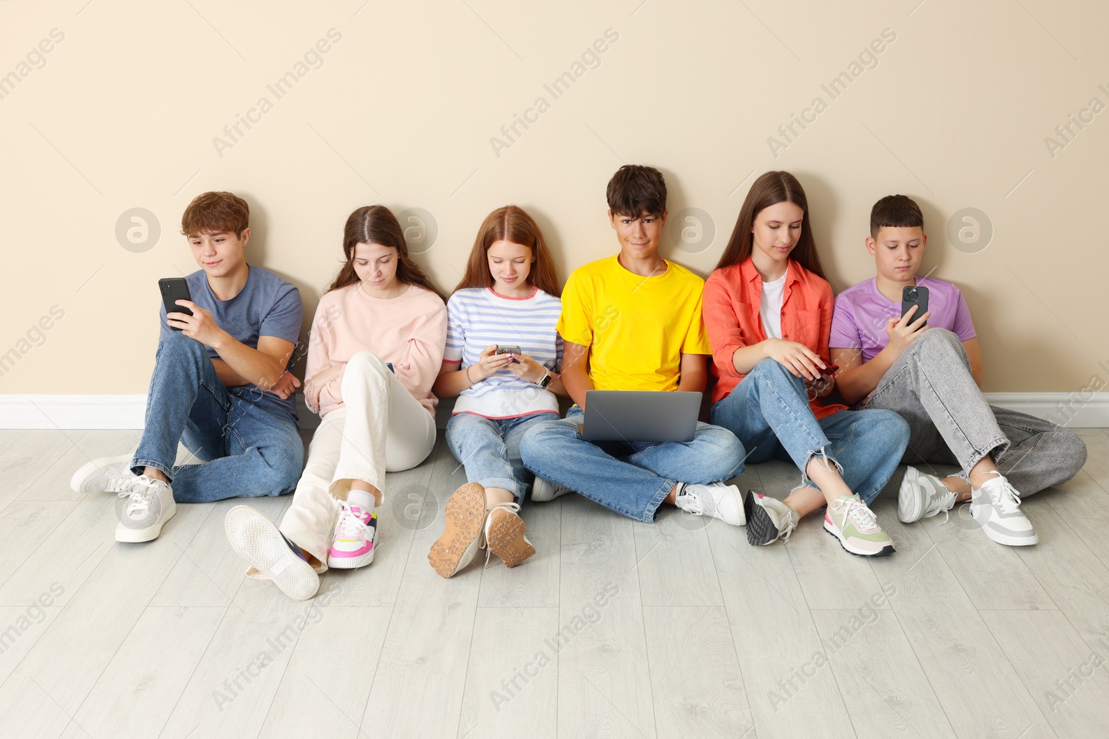 Group of teenagers with laptop and smartphones near beige wall indoors Photo of Group of teenagers with laptop and smartphones near beige wall indoors