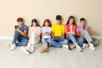 Photo of Group of teenagers with laptop and smartphones near beige wall indoors