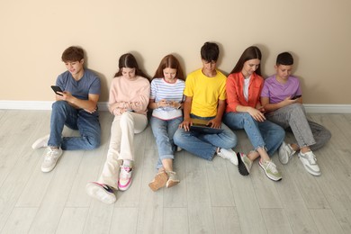 Photo of Group of teenagers with laptop and smartphones near beige wall indoors