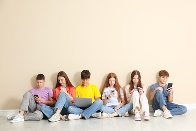 Photo of Group of teenagers with laptop and smartphones near beige wall indoors. Space for text