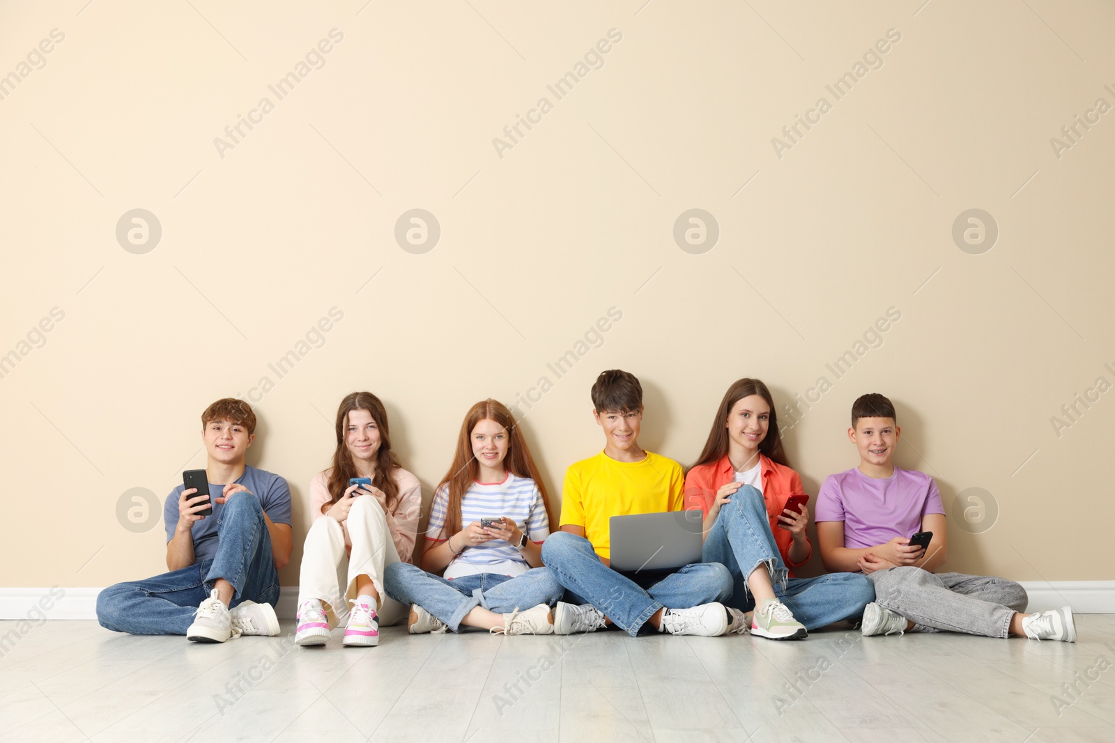 Group of teenagers with laptop and smartphones near beige wall indoors. Space for text Photo of Group of teenagers with laptop and smartphones near beige wall indoors. Space for text