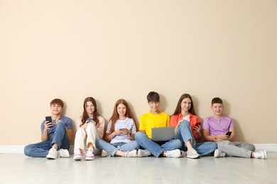 Photo of Group of teenagers with laptop and smartphones near beige wall indoors. Space for text