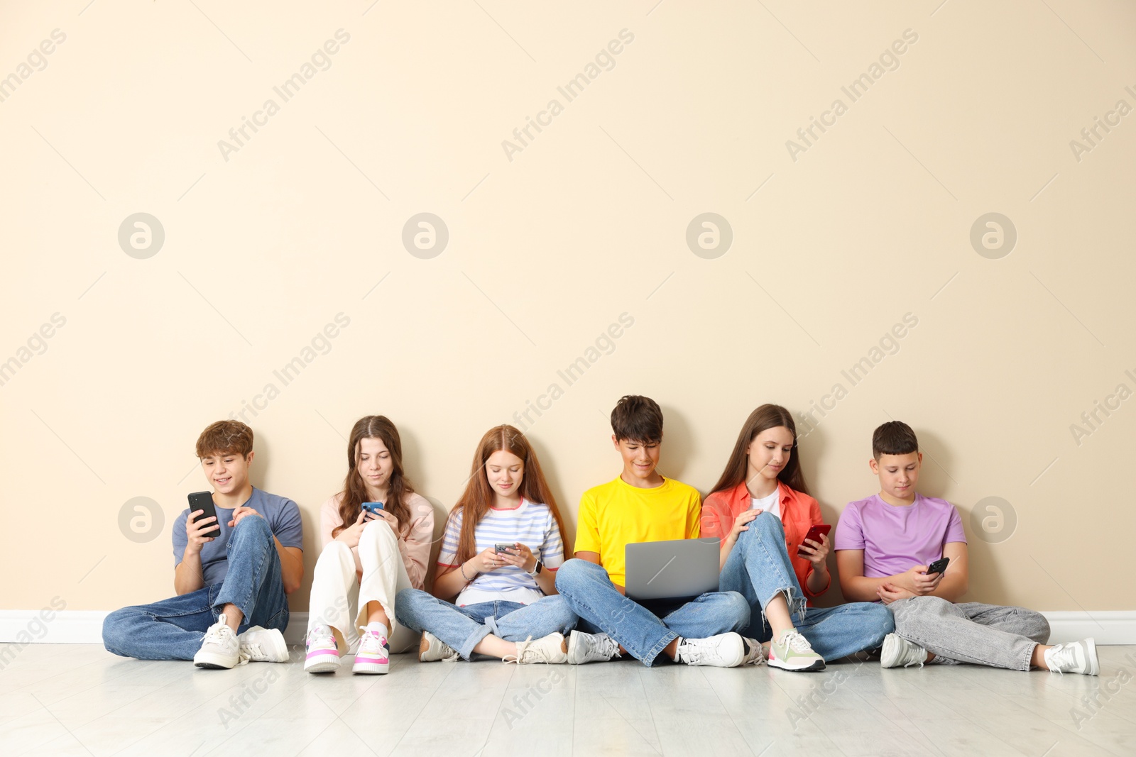 Group of teenagers with laptop and smartphones near beige wall indoors. Space for text Photo of Group of teenagers with laptop and smartphones near beige wall indoors. Space for text