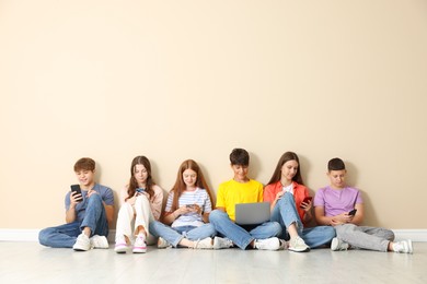 Photo of Group of teenagers with laptop and smartphones near beige wall indoors. Space for text