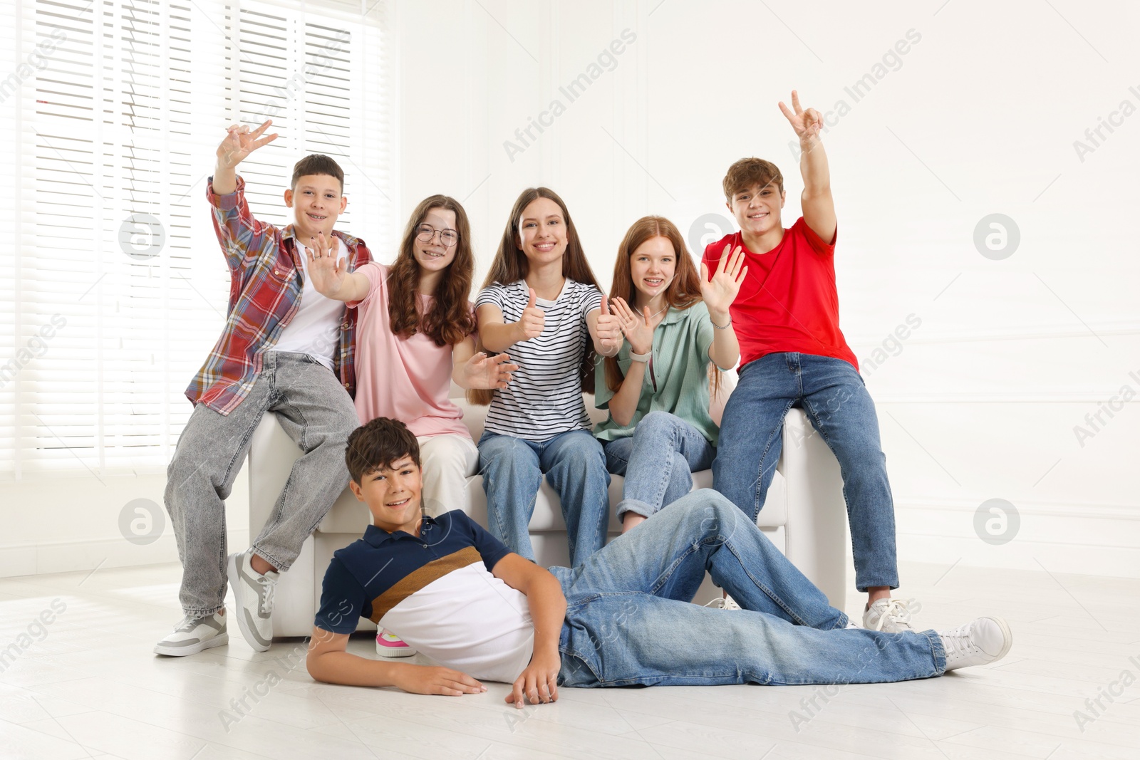 Group of happy teenagers waving on sofa indoors Photo of Group of happy teenagers waving on sofa indoors