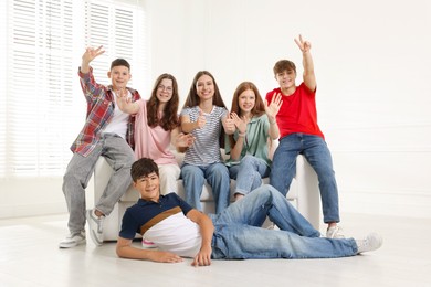 Photo of Group of happy teenagers waving on sofa indoors