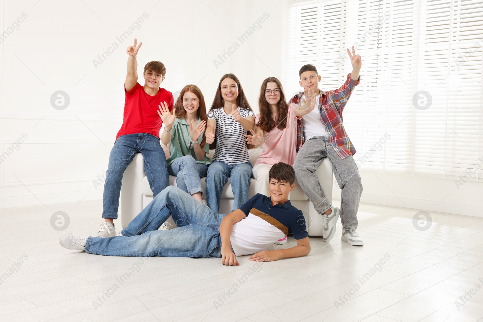 Group of happy teenagers waving on sofa indoors Photo of Group of happy teenagers waving on sofa indoors