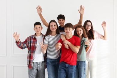 Photo of Group of happy teenagers waving and showing thumbs ups indoors