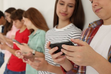 Photo of Teenagers with smartphones near white wall indoors, closeup